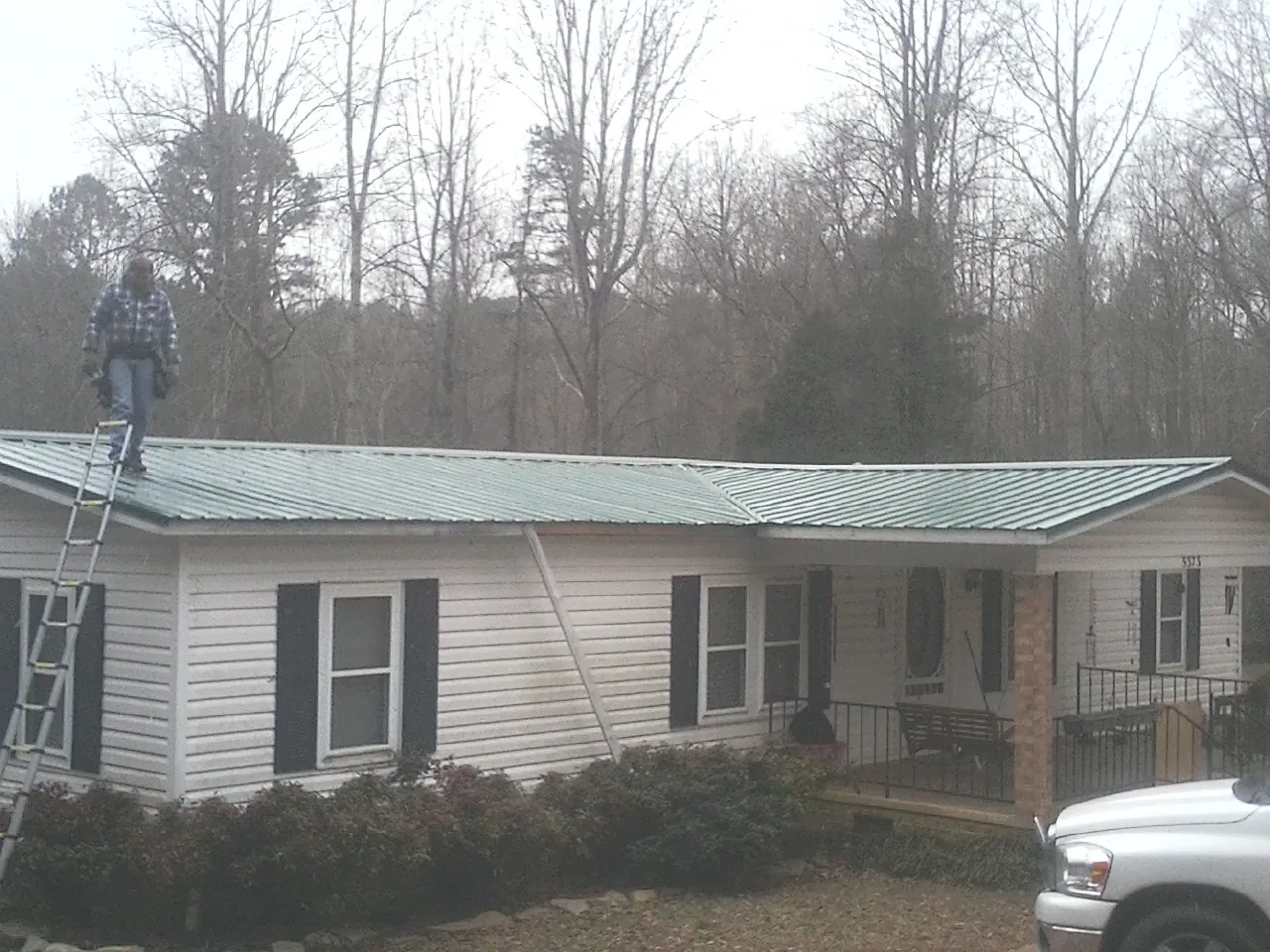 Worker on a ladder beside a new green metal roof on a ranch home in Glenwood
