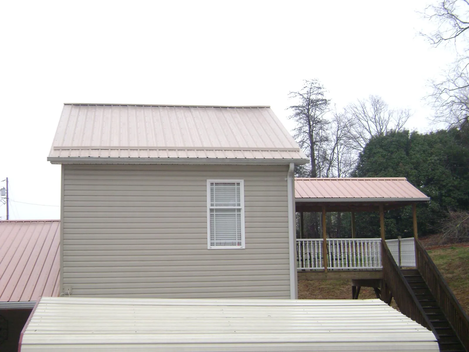 Tan metal roofs on a two story addition and attached porch, from a Roof Replacement job in Glenwood